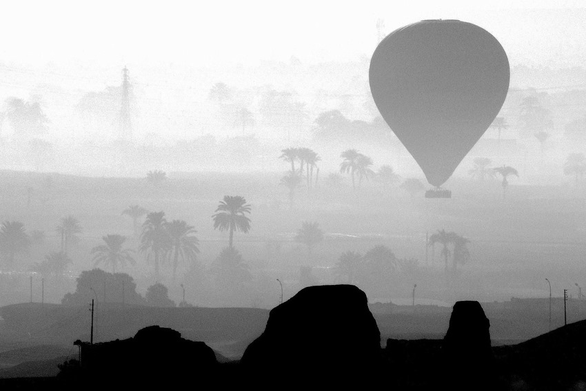 Ballonaufstieg im Niltal Aegypten - im Vordergrund alte Ruinen, darüber der aufsteigende Ballon und im Tal sind mehrere Palmen zu sehen.